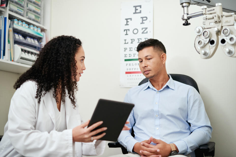 Eye doctor consulting a patient in a clinic with an eye chart on the wall