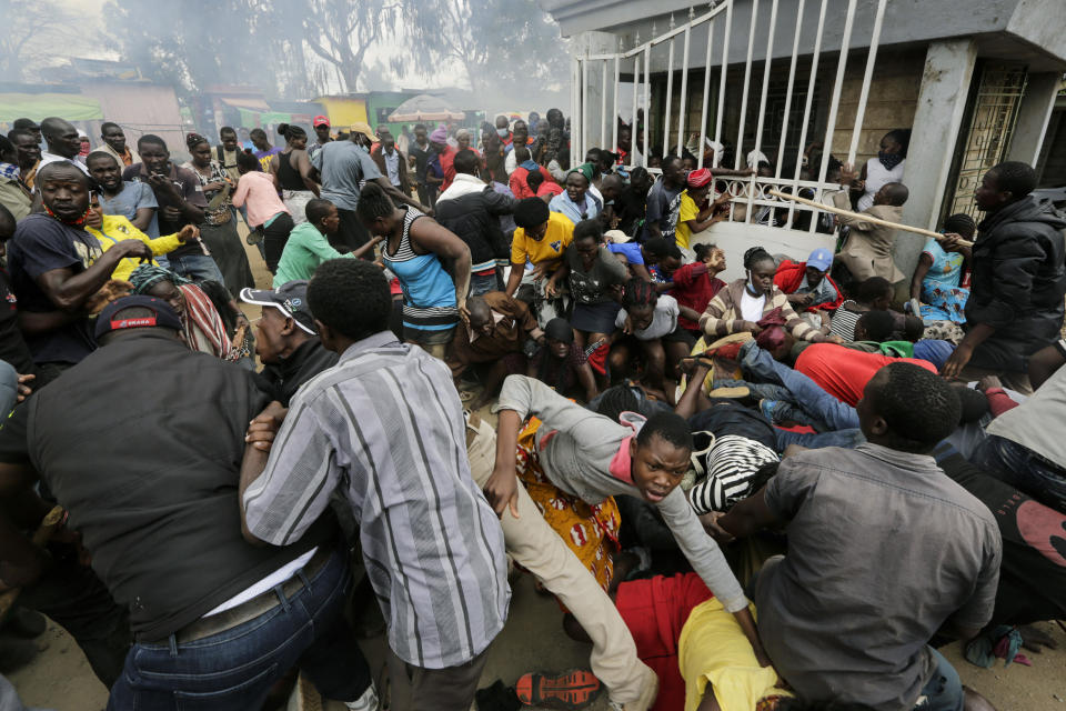 Residents desperate for a planned distribution of food for those suffering under Kenya's coronavirus-related movement restrictions push through a gate and create a stampede, causing police to fire tear gas and leaving several injured, at a district office in the Kibera slum, or informal settlement, of Nairobi, Friday, April 10, 2020. (AP Photo/Khalil Senosi)