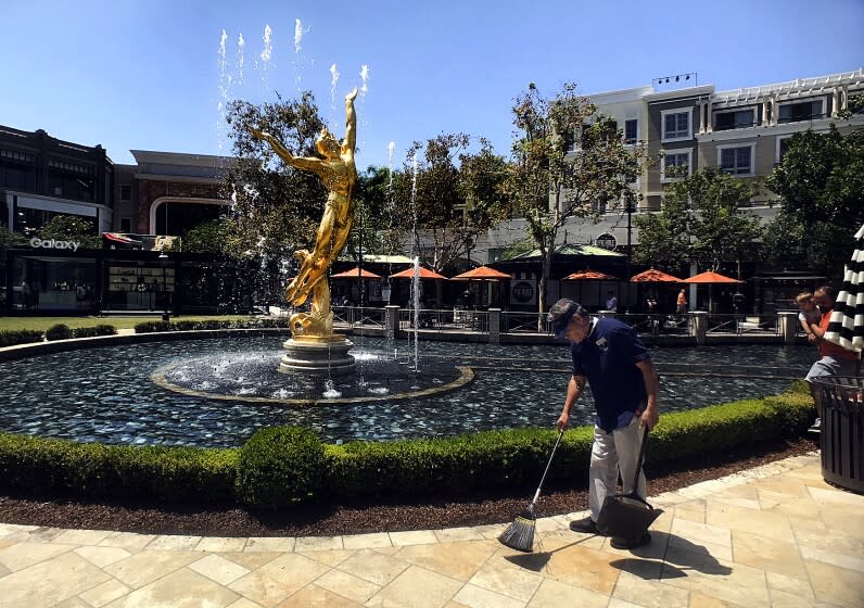 A custodian is seen sweeping before a large fountain bearing a golden sculpture of a soaring nude male figure