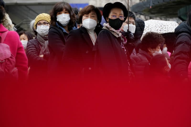 People wearing masks after the coronavirus outbreak wait in a line to buy masks as it rains in front of a department store in Seoul