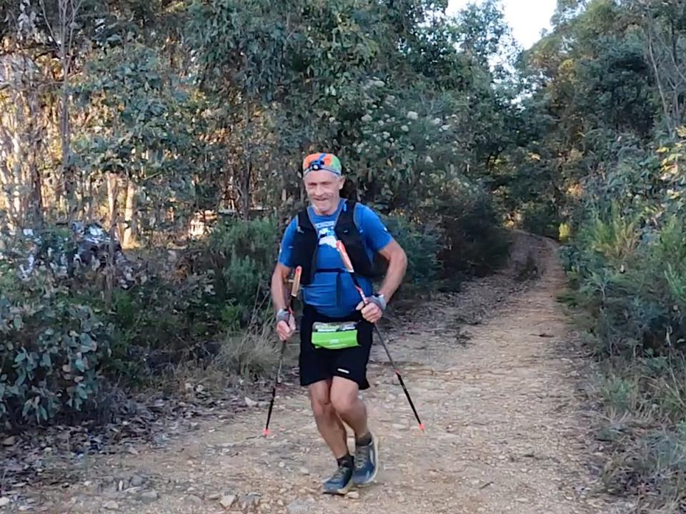 John Salton running through a trail with walking sticks.