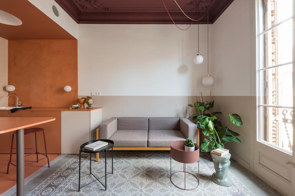 A color shift happens on the opposing side of the kitchen in the living space, where a dark blush shade creates a vertical “horizon” around the room. A Kettal Landscape sofa is accompanied by a Ferm Living planter and suspended globe lights. The original floors were intact, and its light shade foils the deep burgundy on the ceiling. “One of the Art Nouveau corner plaster motifs on the ceiling had to be replaced due to the fire,” Andrea says.