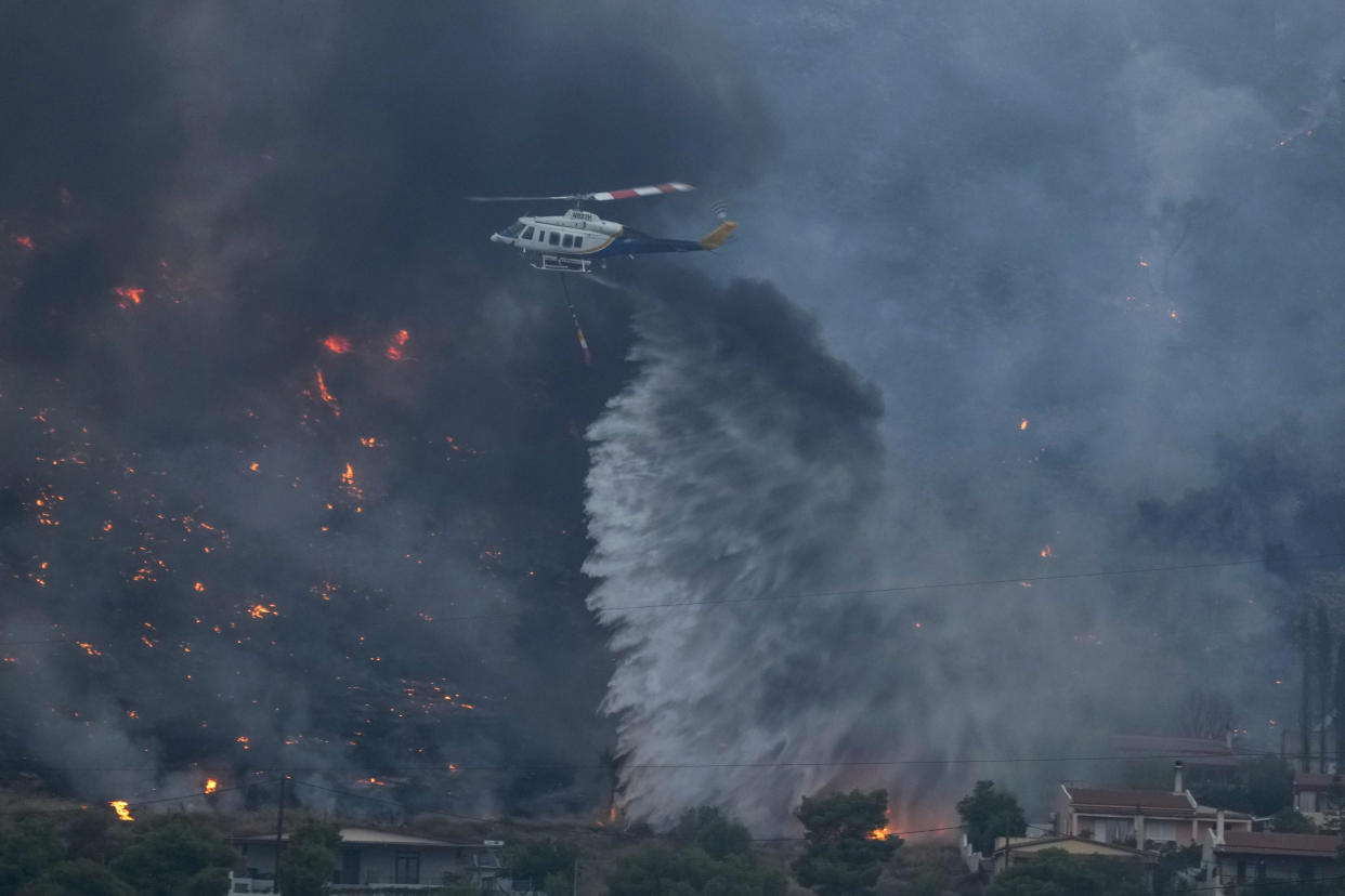 A firefighting helicopter dumps water on houses in Kalamaki,