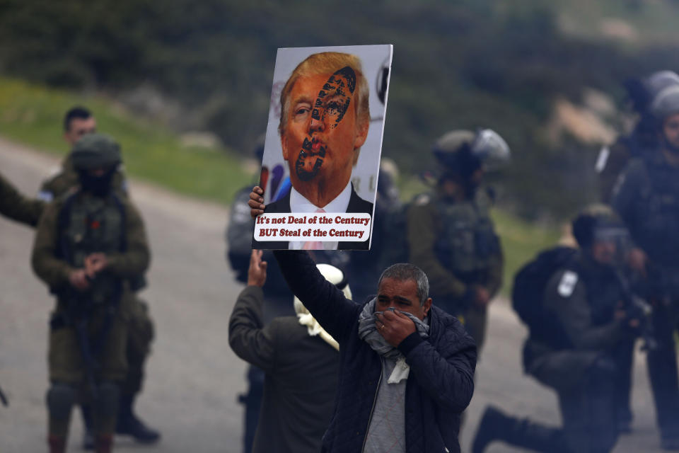 File - In this Tuesday, Feb. 25, 2020 file photo, a Palestinian demonstrator covers his face from tear gas fired by Israeli forces as he holds a poster of -U.S. President Donald Trump during a protest against President Donald Trump's Mideast initiative, in Jordan Valley in the West Bank. Israeli Prime Minister Benjamin Netanyahu has vowed to annex the valley and all of Israel's far-flung West Bank settlements, in line with President Donald Trump's Middle East plan, which overwhelmingly favors Israel and has been rejected by the Palestinians. (AP Photo/Majdi Mohammed, File)