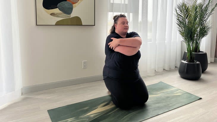 Woman kneeling on a yoga mat taking a body-positive yoga variation to Eagle arms by crossing her arms in front of her chest