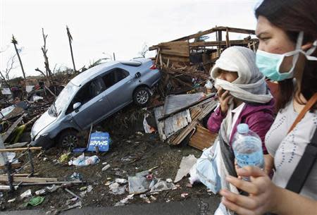 People covering their faces pass a car in debris after super typhoon Haiyan battered Tacloban City, in central Philippines November 13, 2013. REUTERS/Edgar Su