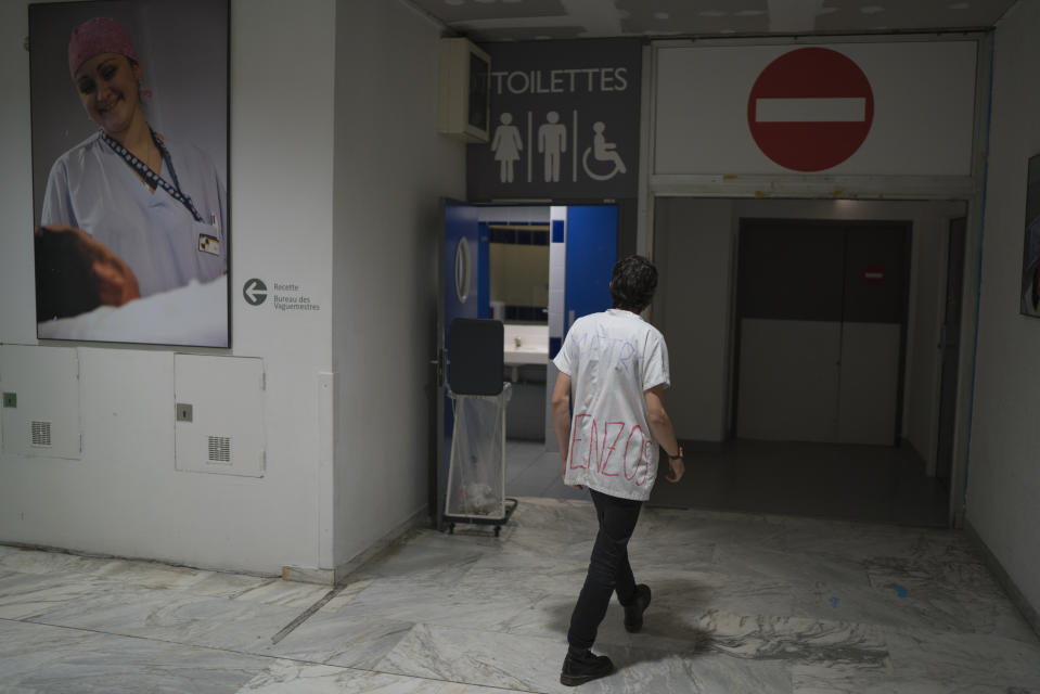 In this photo taken on Dec.15, 2019, a hospital intern wears a work uniform that reads "metro, work, Benzedrine" in the lobby of La Timone hospital during his sixth day on strike, in Marseille, southern France. In a hospital in Marseille, student doctors are holding an exceptional, open-ended strike to demand a better future. France’s vaunted public hospital system is increasingly stretched to its limits after years of cost cuts, and the interns at La Timone - one of the country’s biggest hospitals - say their internships are failing to prepare them as medical professionals. Instead, the doctors-in-training are being used to fill the gaps. (AP Photo/Daniel Cole)