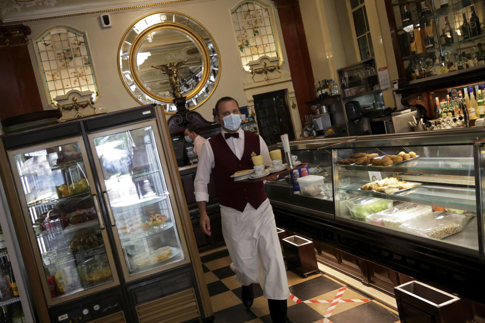 A waiter wearing a face mask carries a tray at the Versailles restaurant and pastry shop in Lisbon, Monday, May 18, 2020. Some cafes and restaurants are reopening in Portugal on Monday. The government is gradually easing measures introduced to stem the spread of the new coronavirus. (AP Photo/Armando Franca)