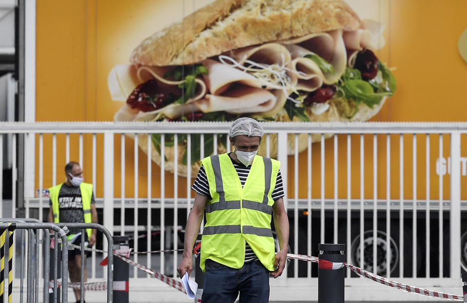 A worker with a face masks walks in front of a meat truck at the Toennies meatpacking plant, Europe's biggest slaughterhouse, where the German Bundeswehr army helps to build up a test center for coronavirus in Rheda-Wiedenbrueck, Germany, Friday, June 19, 2020. Hundreds of new COVID-19 cases are linked to a large meatpacking plant, officials ordered the closure of the slaughterhouse, as well as isolation and tests for everyone else who had worked at the Toennies site — putting about 7,000 people under quarantine. (AP Photo/Martin Meissner)