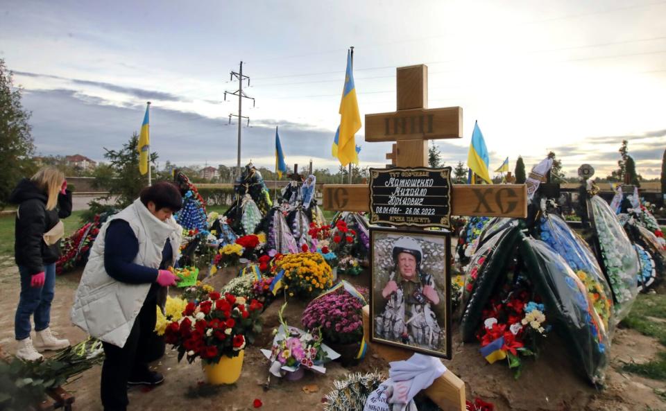 Two women visit graves decorated with flowers, crosses and other items