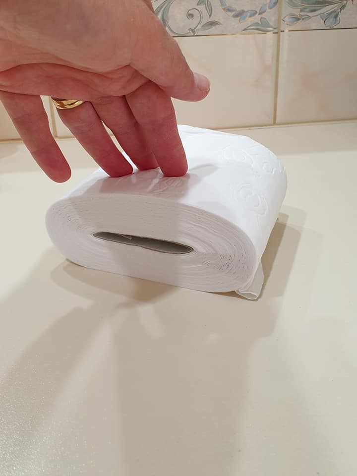 Hand with wedding ring compresses toilet paper roll, hack to extend supply