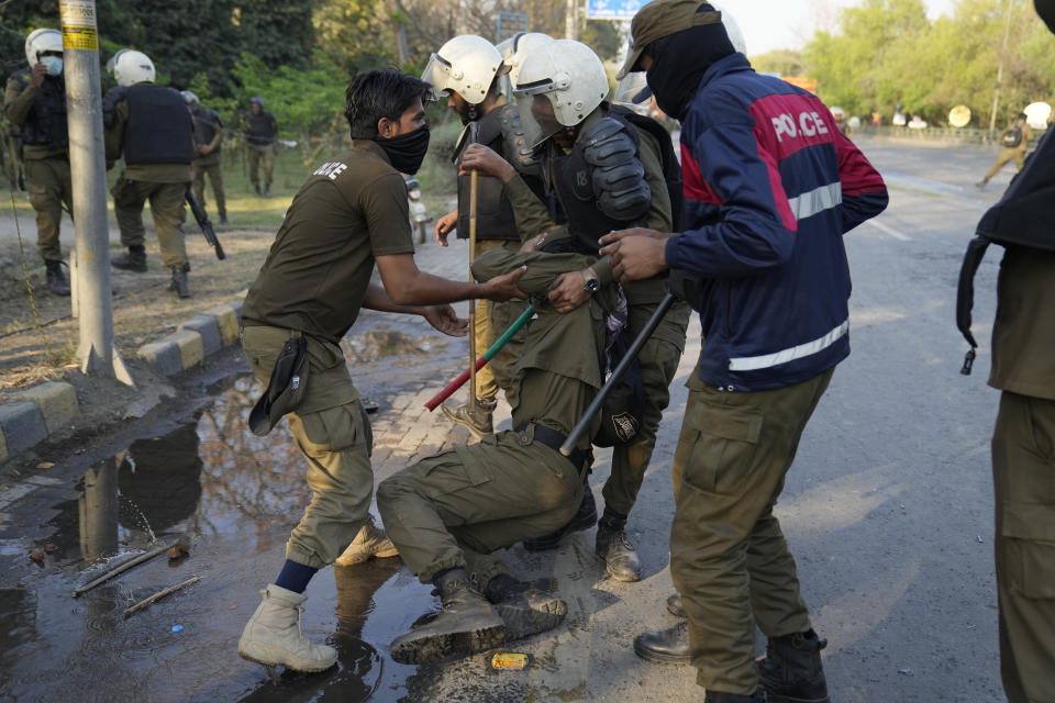 Police officers help their colleague injured in the clashes with the supporters of Pakistan's former Prime Minister Imran Khan, in Lahore, Pakistan, Wednesday, March 8, 2023. Pakistani police used water cannons and fired tear gas to disperse supporters of the country's former Prime Minister Khan Wednesday in the eastern city of Lahore. Two dozen Khan supporters were arrested for defying a government ban on holding rallies, police said. (AP Photo/K.M. Chaudary)