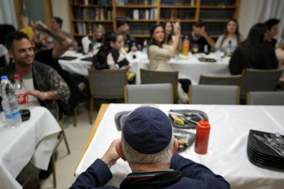 A man eats as young people enjoy music at a meal at Cyprus' Jewish Community Center before their return to Israel, in the southern coastal town of Larnaca, Cyprus, on Thursday, Nov. 30, 2023. Attendants are among a group of 70 people who attended a retreat in Cyprus to help them cope with the psychological trauma they suffered from that attack. (AP Photo/Petros Karadjias)