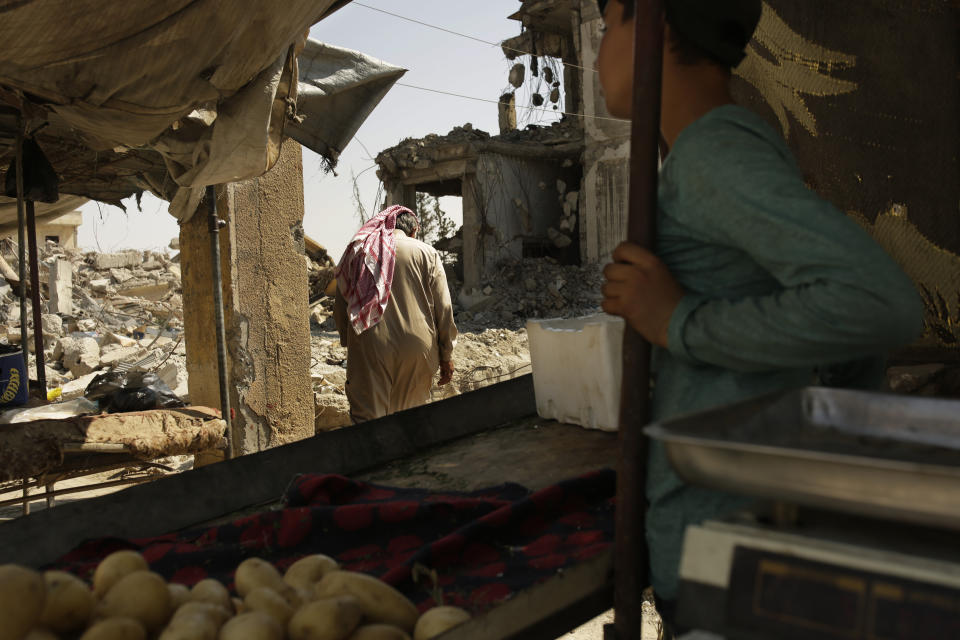 In this Thursday, Sept. 5, 2019, photo, a man passes through a vegetable stand on the way to his heavily damaged home in Raqqa, Syria. Officials say more than 800,000 people have returned to the city and its adjacent suburbs_ nearly eight times the residents who were left when Islamic State militants were finally expelled from its stronghold in Oct. 2017. (AP Photo/Maya Alleruzzo)