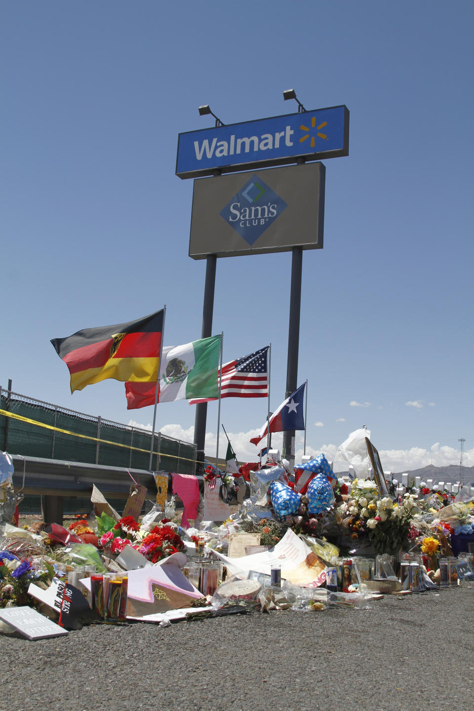 In this Aug. 12, 2019 photo, mourners visit the makeshift memorial near the Walmart in El Paso, Texas, where 22 people were killed in a mass shooting that police are investigating as a terrorist attack targeting Latinos. The flags show the nationalities of those killed in the attack, including a German man who lived in nearby Ciudad Juarez, Mexico. On Thursday, Aug. 22, 2019, Walmart said it plans to reopen the El Paso store where 22 people were killed in a mass shooting, but the entire interior of the building will first be rebuilt. (AP Photo/Cedar Attanasio)