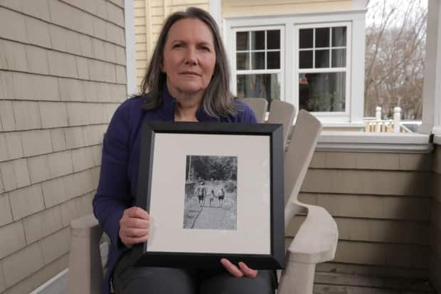 Dianne Taylor holds a photo of her with her late husband, Tim Taylor, and their daughter. Tim died suddenly of cancer in August 2018. (Dave Laughlin/CBC - image credit)