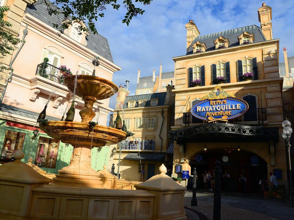 Ground view of a fountain, old bildings, and Remy's Ratatouille Adventure building entrance.