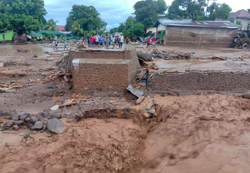 People inspect damaged buildings at a village hit by flash flood in East Flores, Indonesia, Sunday, April 4, 2021. Landslides and flash floods from torrential rains in eastern Indonesia have killed a number of people and displaced thousands, the disaster agency said Sunday. (AP Photo/Ola Adonara)