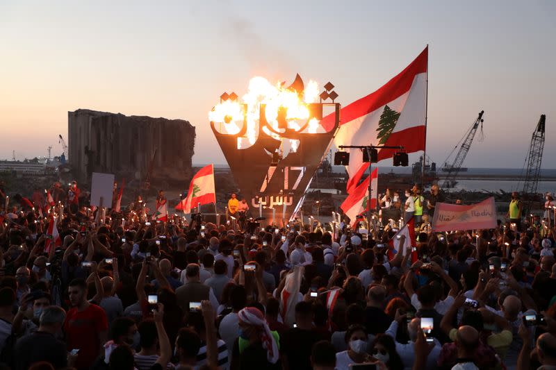 Anti-government demonstrators take pictures of a metal sculpture spelling out the word "revolution" topped by flames during a protest as Lebanese mark one year since the start of nation-wide protests, near Beirut's port