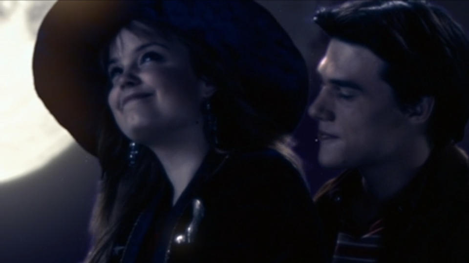 Kimberly J. Brown as Marnie Piper wears a wide brim hat and smiles at the night sky with Finn Wittrock as Cody behind her in "Halloweentown High"