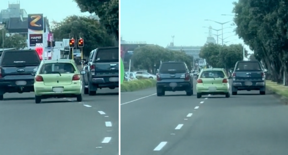 Image of the small, green car driving in the middle of two lanes between two large black vehicles.