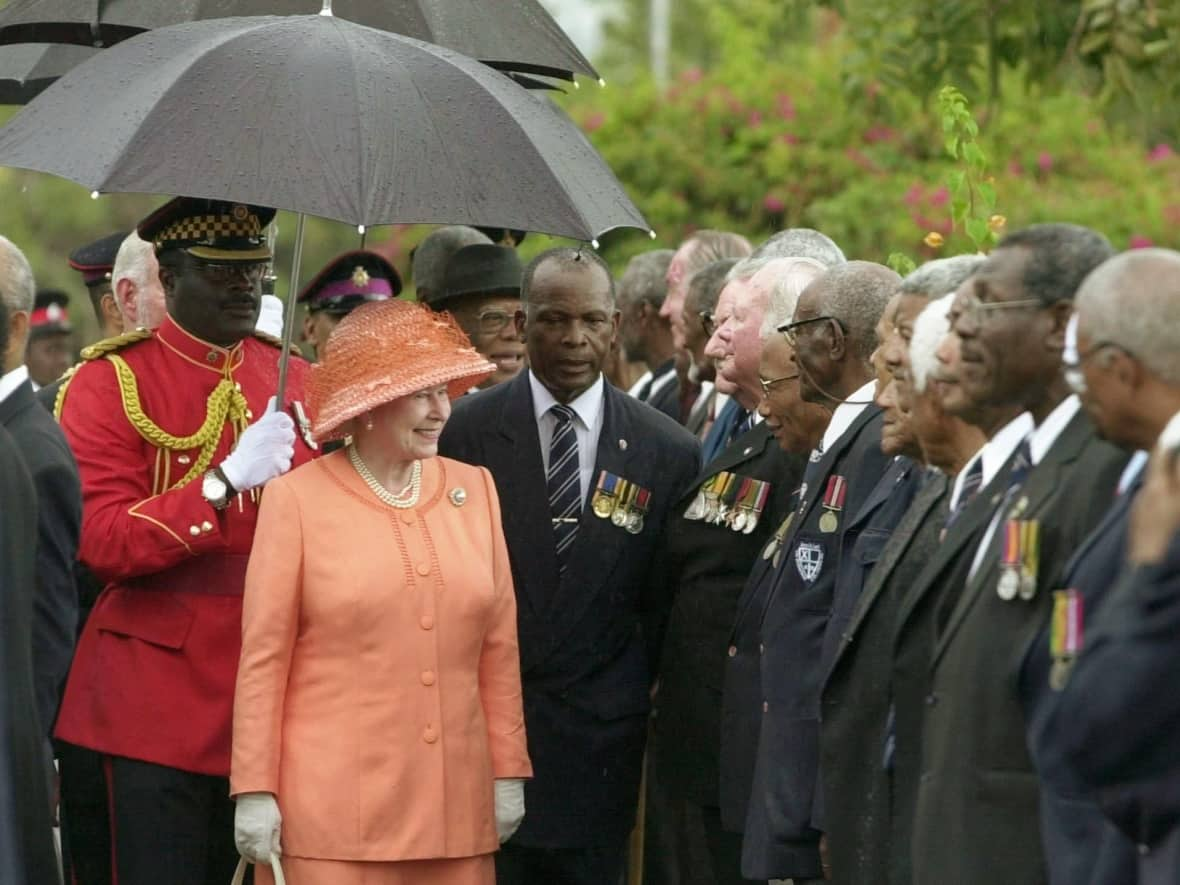 Queen Elizabeth greets a group of Jamaican war veterans in Kingston in 2001 during a visit to mark her golden jubilee year. There have been mixed reactions to her passing among those in the Caribbean diaspora, where discussion about cutting ties with the monarchy have been more frequent of late.  (Lynne Sladky/Associated Press - image credit)