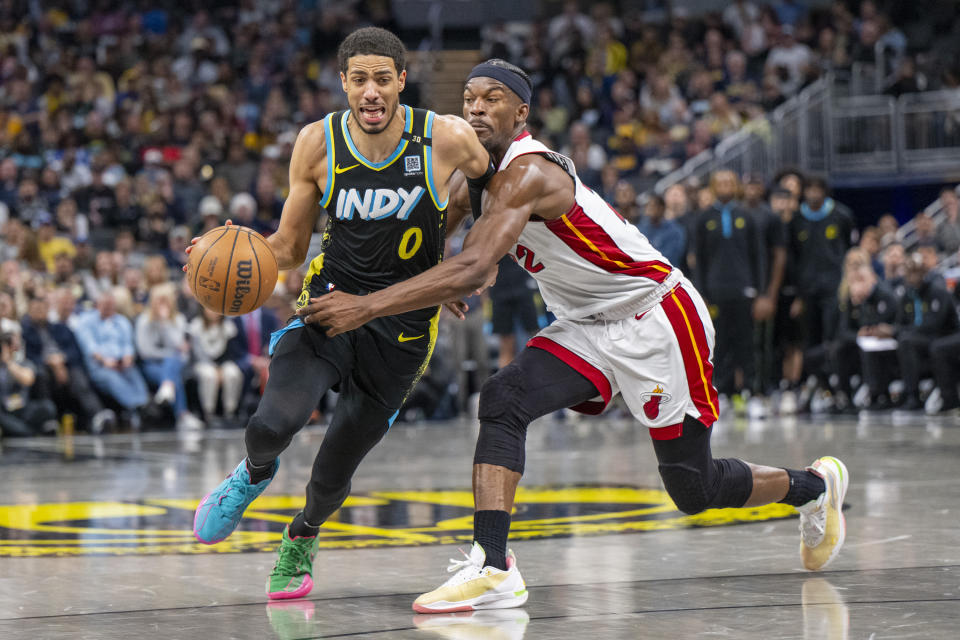 Indiana Pacers guard Tyrese Haliburton (0) drives against the defense of Miami Heat forward Jimmy Butler, right, during the second half of an NBA basketball game in Indianapolis, Sunday, April 7, 2024. (AP Photo/Doug McSchooler)