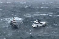 In this photo provided by the U.S. Coast Guard Pacific Northwest, a Coast Guard ship, left, attempts to a rescue a distressed yacht at the mouth of the Columbia River between Oregon and Washington state on Friday, Feb. 3, 2023. A newly minted Coast Guard rescue swimmer saved the life of a man who was piloting the yacht. (AET1 Kyle Turcotte/U.S. Coast Guard Pacific Northwest via AP)