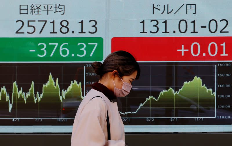 A woman walks past an electric board showing Nikkei index and exchange rate between Japanese Yen and U.S. dollar outside a brokerage at a business district in Tokyo