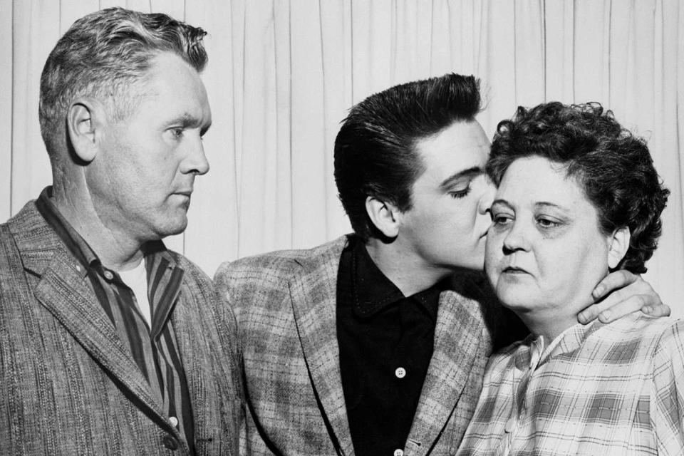 Singer Elvis Presley kisses his mother, Gladys, on the eve of his induction into the Army. At left is his father, Vernon.