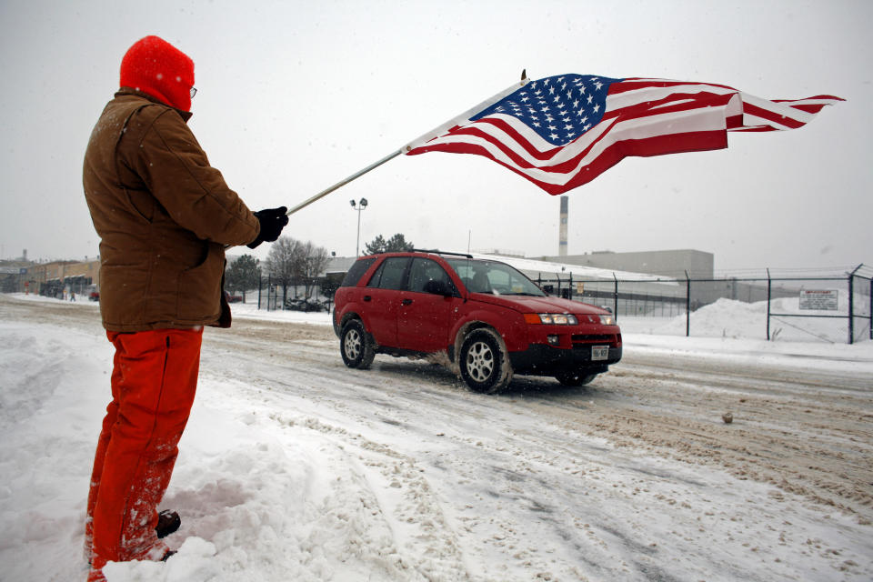 JANESVILLE, WI - 23 DE DICIEMBRE: El residente Billy Bob Grahn sostiene una bandera estadounidense para mostrar su apoyo mientras los trabajadores restantes en una planta de General Motors se van después de su último turno el 23 de diciembre de 2008 en Janesville Wisconsin.  Después de más de 85 años fabricando vehículos, la fábrica de Janesville cerró después de enviar sus últimos SUV Chevrolet y GMC, dejando a más de 1.200 trabajadores sin trabajo.  (Foto de Darren Hauck/Getty Images)