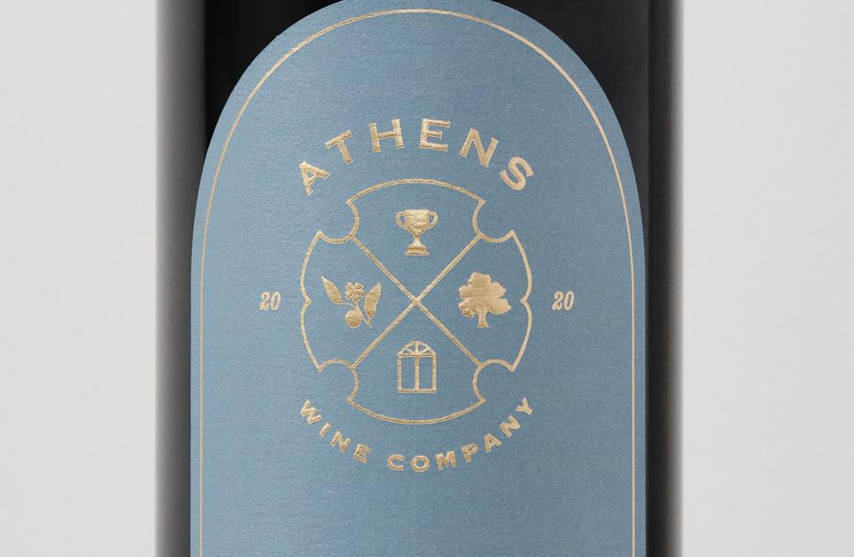 This promotional photo from Athens Wine Company shows a bottle of Cabernet Sauvignon with symbols representing a football trophy, the Tree That Owns Itself, the Georgia state flag arch and a peach blossom.