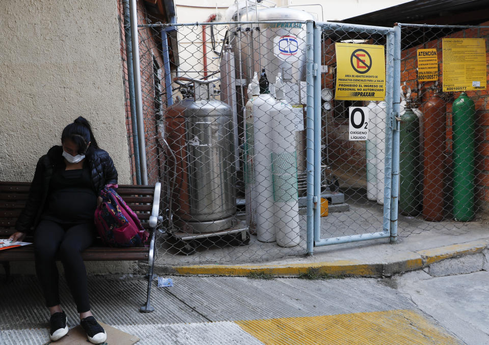 A pregnant woman waiting to be attended sits on a bench situated next to an oxygen tank storage area, outside the Women's Hospital, in La Paz, Bolivia, Thursday, Aug. 13, 2020. Doctors say the supply of oxygen for babies in the intensive care unit is becoming scarce, the result of nationwide blockades by supporters of the party of former President Evo Morales who object to the recent postponement of elections. Bolivia's political and social crisis is coinciding with the continued spread of the new coronavirus. (AP Photo/Juan Karita)