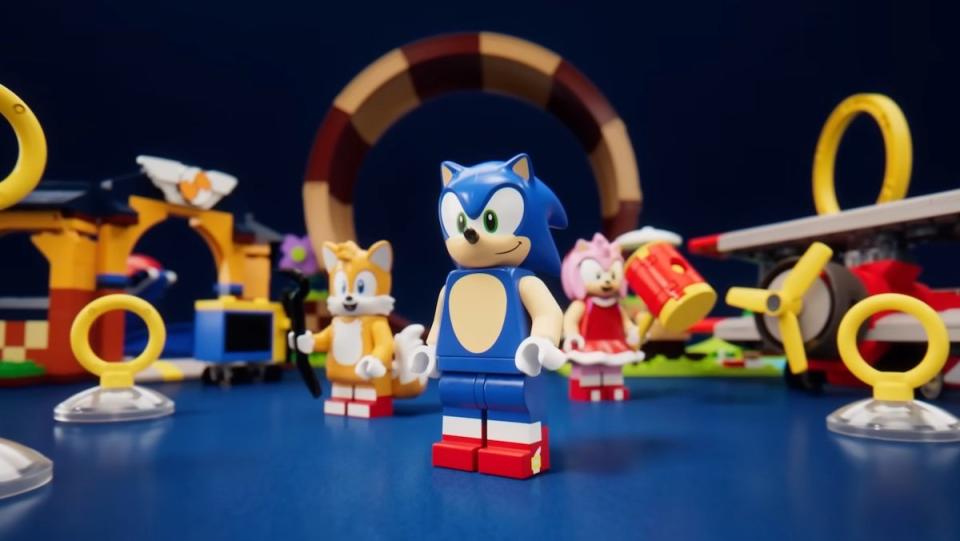 Sonic, Tails, and Amy LEGO minifigs standing in front of sets based on the Sonic games