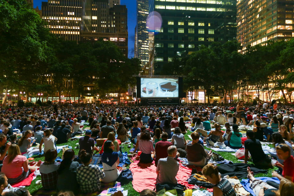 Outdoor movie screening event with large audience sitting on blankets in a park at dusk