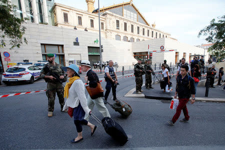 Travellers walk past French police and soldiers who secure a street near the Saint-Charles train station (Rear) after French soldiers shot and killed a man who stabbed two women to death at the main train station in Marseille, France, October 1, 2017. REUTERS/Jean-Paul Pelissier