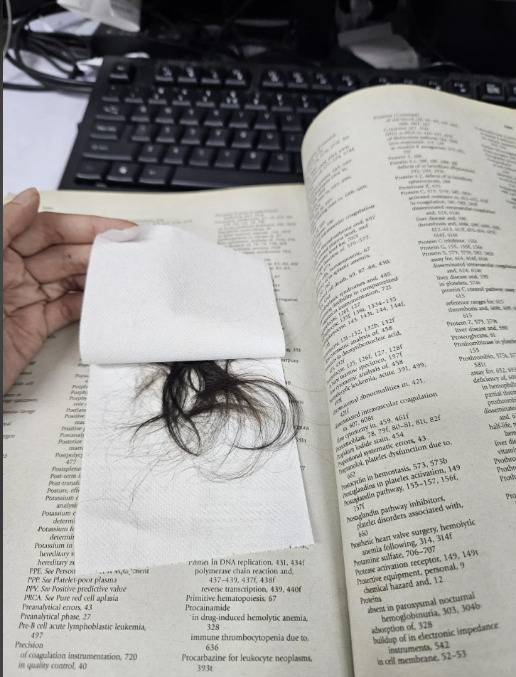 Person holding a napkin with strands of hair on an open scientific textbook