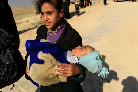 A displaced Iraqi girl, who fled her home during a battle between Iraqi forces and Islamic State militants, carries a child in Mosul, Iraq March 9, 2017. REUTERS/Thaier Al-Sudani