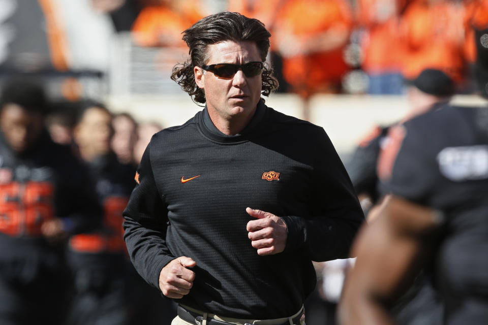 FILE - In this Nov. 2, 2019, file photo, Oklahoma State coach Mike Gundy runs onto the field before the team's NCAA college football game against TCU in Stillwater, Okla. Hubbard said on Twitter that he won’t do anything with the program until there is change after Gundy was photographed wearing a T-shirt representing far-right online publication One America News Network. Gundy is seen in a photograph on Twitter wearing the T-shirt with the letters OAN. (AP Photo/Sue Ogrocki, File)