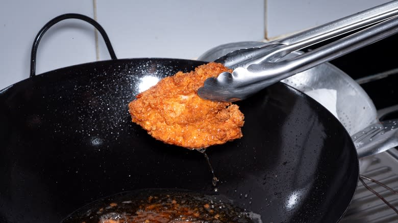 Tongs removing fried chicken from oil over a wok