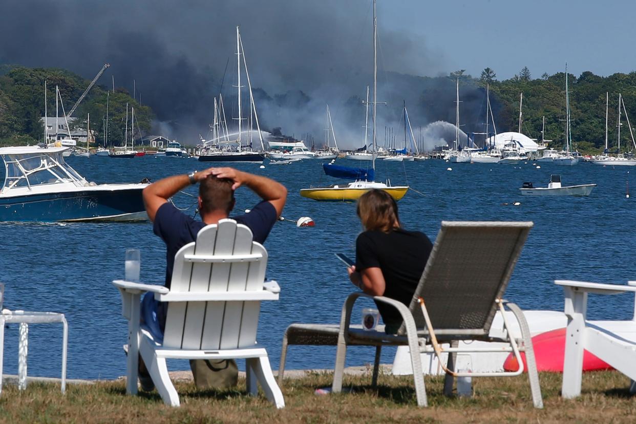 People look across Mattapoisett harbor at a multi-alarm fire ripping through the Mattapoisett Boat Yard on Ned's Point Road in Mattapoisett on Friday, Aug. 19, 2022.