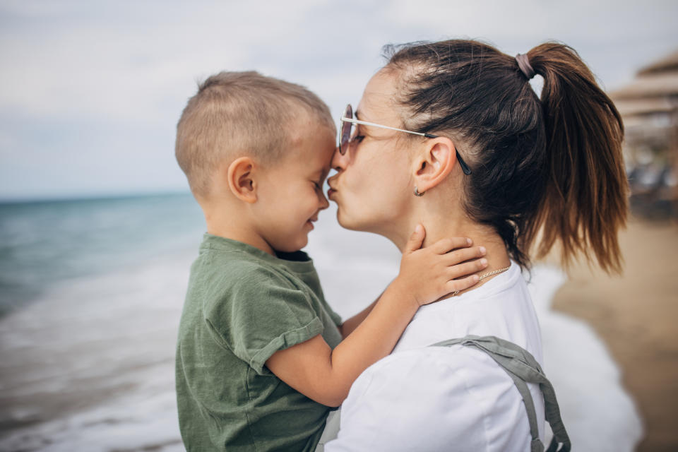 a woman holding her son and kissing his head on the beach