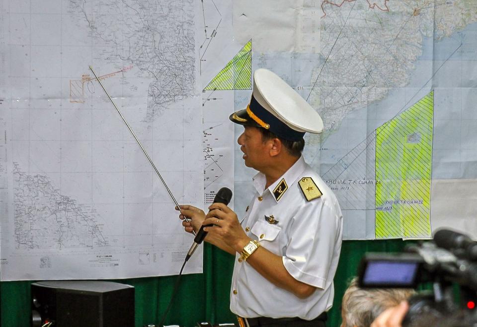 a map in a naval uniform points to a map with a pointer and speaks into a microphone