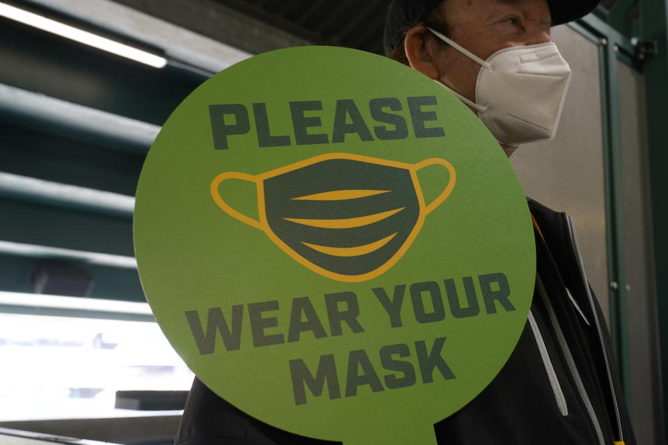 FILE - In this April 3, 2021, file photo, stadium worker holds up a sign for people to wear face masks before a baseball game between the Oakland Athletics and the Houston Astros in Oakland, Calif. As the world struggles to break the grip of COVID-19, psychologists and misinformation experts are studying why the pandemic spawned so many conspiracy theories, which have led people to eschew masks, social distancing and vaccines. (AP Photo/Jeff Chiu, File)