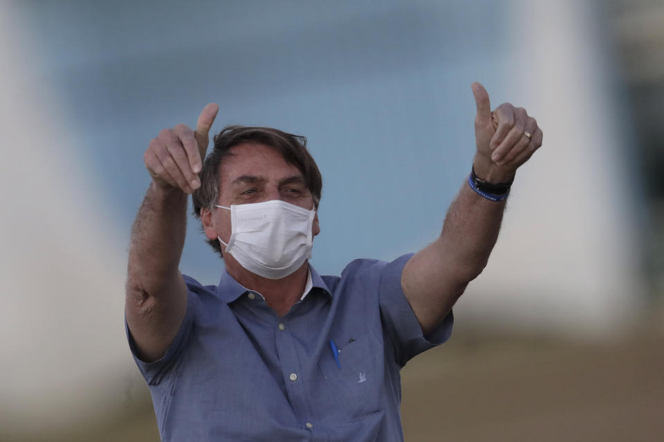 Brazil's President Jair Bolsonaro who is infected with COVID-19, wears a protective face mask as he flashes thumbs up at supporters during a Brazilian flag retreat ceremony outside his official residence Alvorada Palace, in Brasilia, Brazil, Friday, July 17, 2020. On Thursday evening, the federal health ministry reported that the country had passed 2 million confirmed cases of virus infections and 76,000 deaths. (AP Photo/Eraldo Peres)