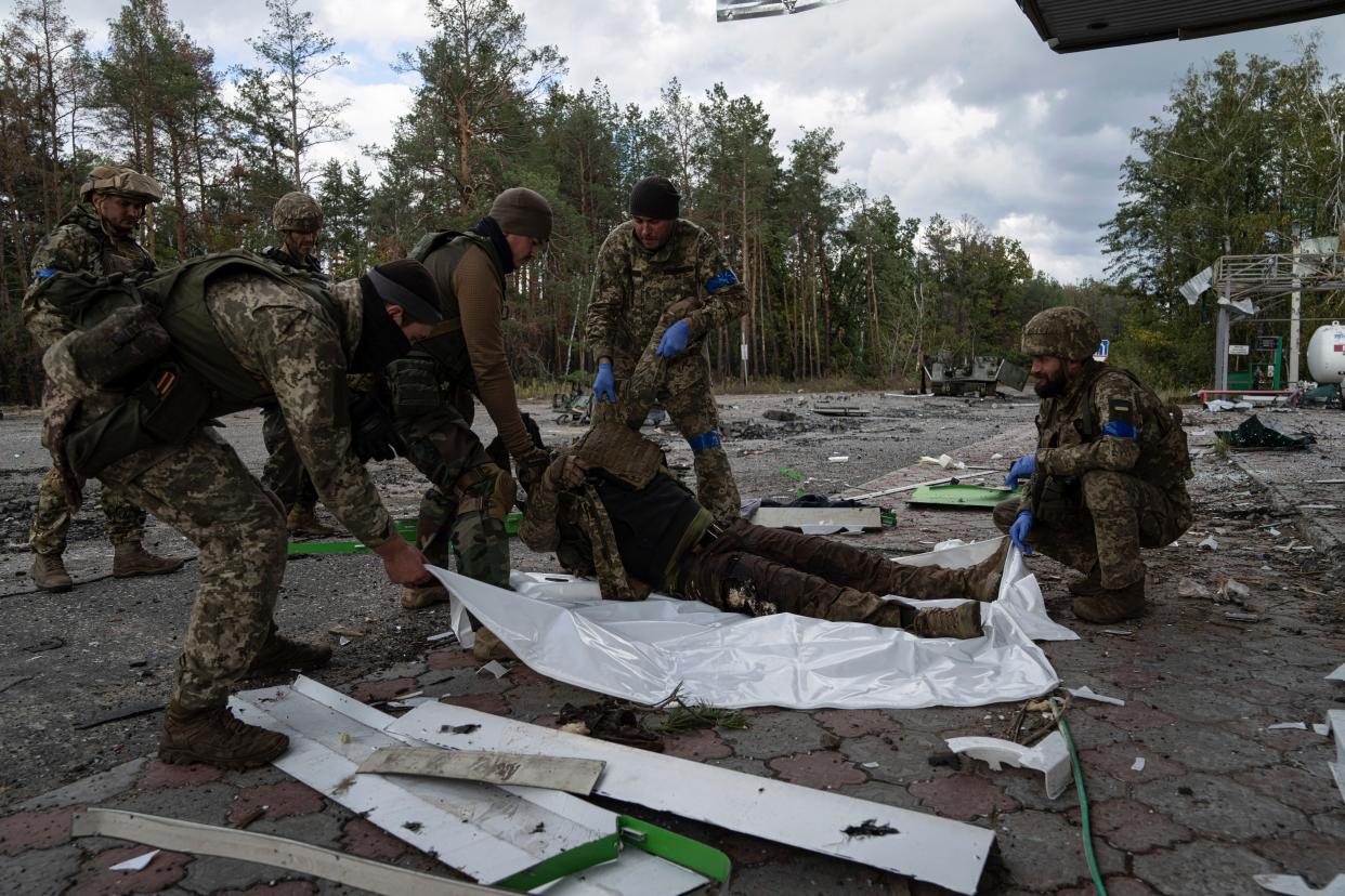 Ukrainian servicemen put in a plastic bag a dead body of their comrade in the recently recaptured town of Lyman, Ukraine, Monday, Oct. 3, 2022.