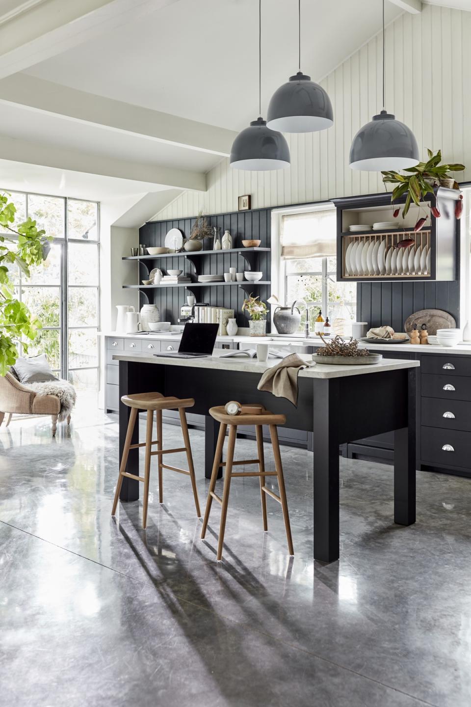 Kitchen island ideas in dark gray with two wooden stools, in a room with high ceilings and gray stone flooring.