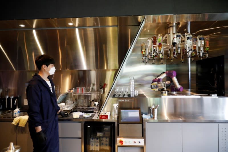 Drink Bot makes a cocktail as an employee wearing a mask to avoid the spread of the coronavirus disease (COVID-19) looks on at a cafe in Seoul