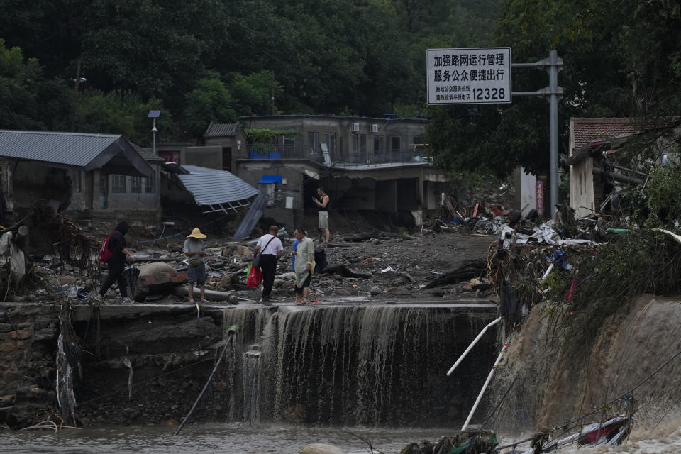 People walk through a village damaged by floodwaters in the Mentougou District as continuous rainfall triggers alerts in Beijing, Monday, July 31, 2023. (AP Photo/Andy Wong)