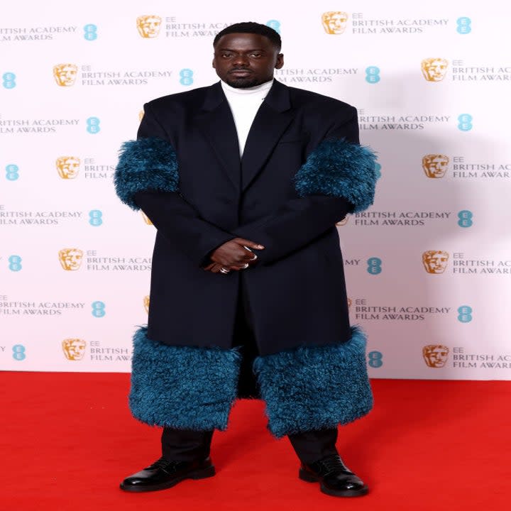 Daniel Kaluuya in a long coat with a wide, furry trim on the bottom and at the elbows on the 2022 BAFTAs red carpet